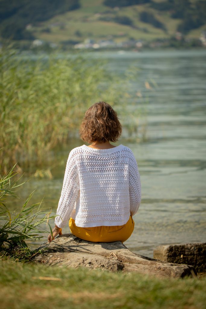 Frau sitzt am Seeufer und blickt entspannt aufs Wasser